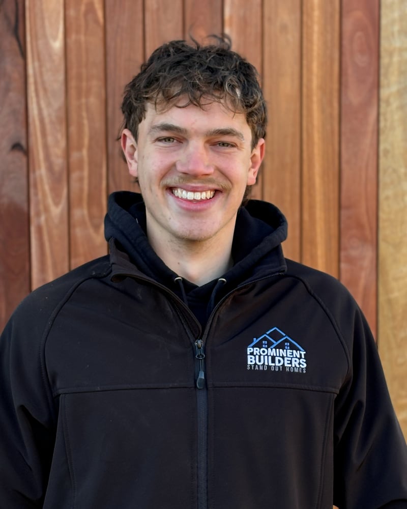 Lachy, apprentice carpenter at Prominent Builders, in a branded jacket against timber cladding