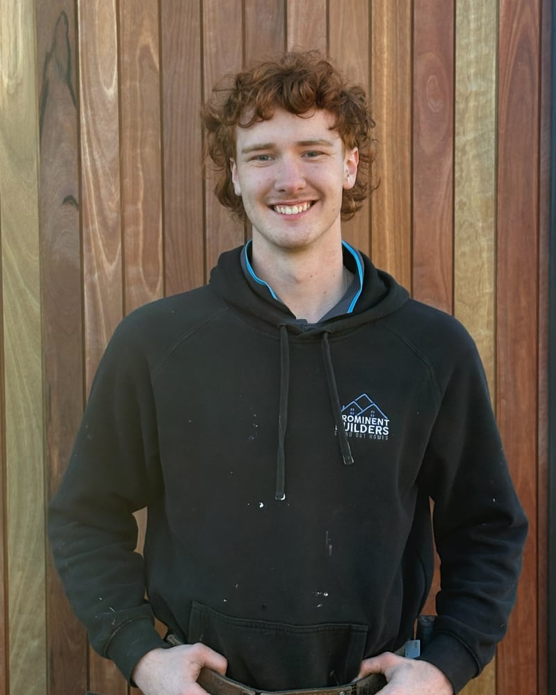 Levi, apprentice carpenter at Prominent Builders, in a branded hoodie and tool belt against timber cladding