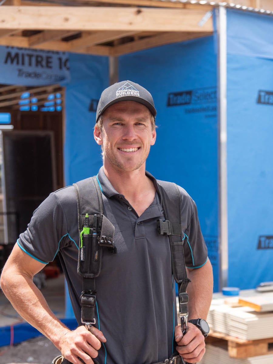 Nathanael Furlong, Director and Head Carpenter at Prominent Builders, in a Prominent Builders polo and tool harness against timber cladding