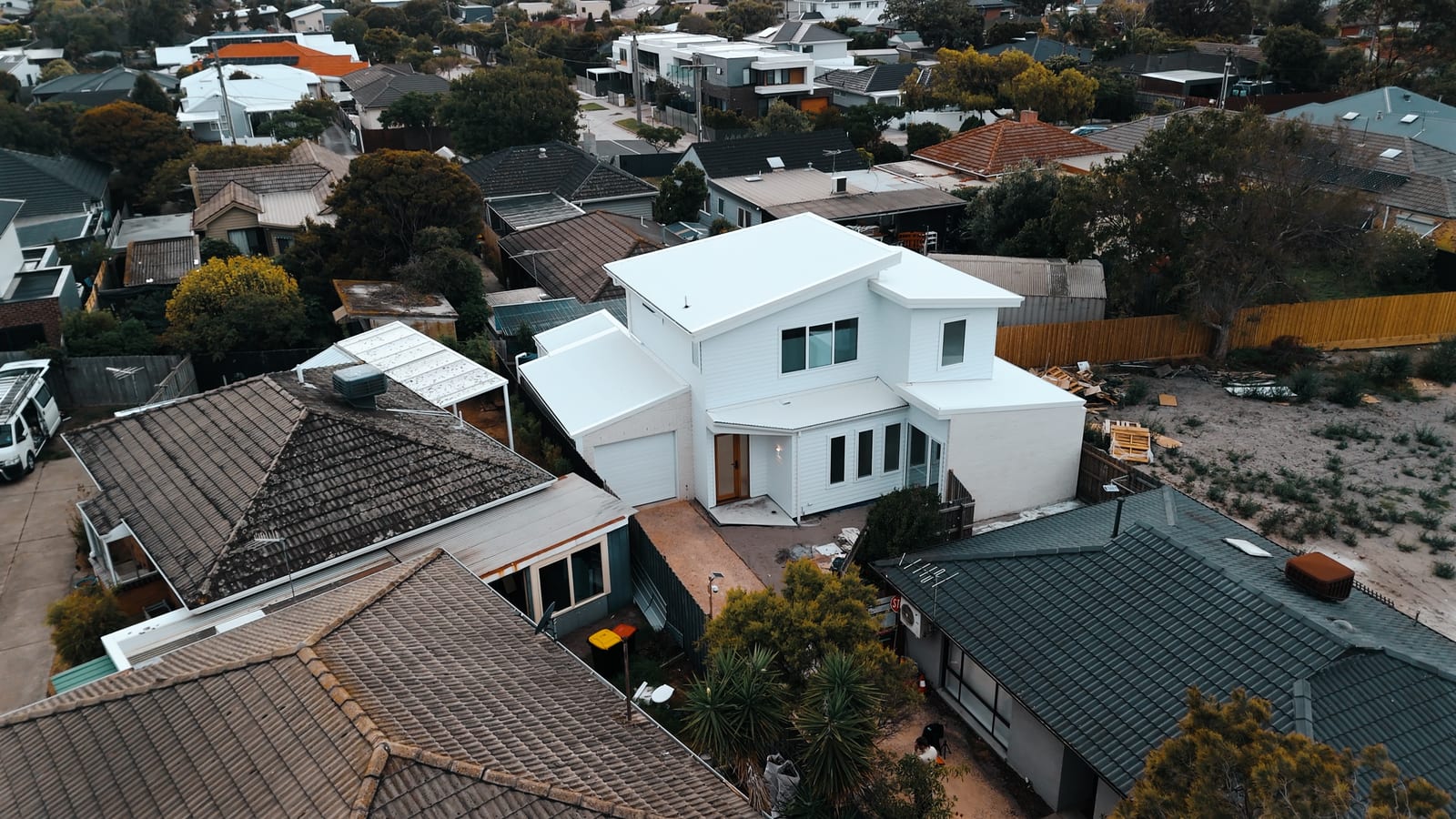 Aerial view of the finished white weatherboard home among older tile-roofed neighbours on a narrow block