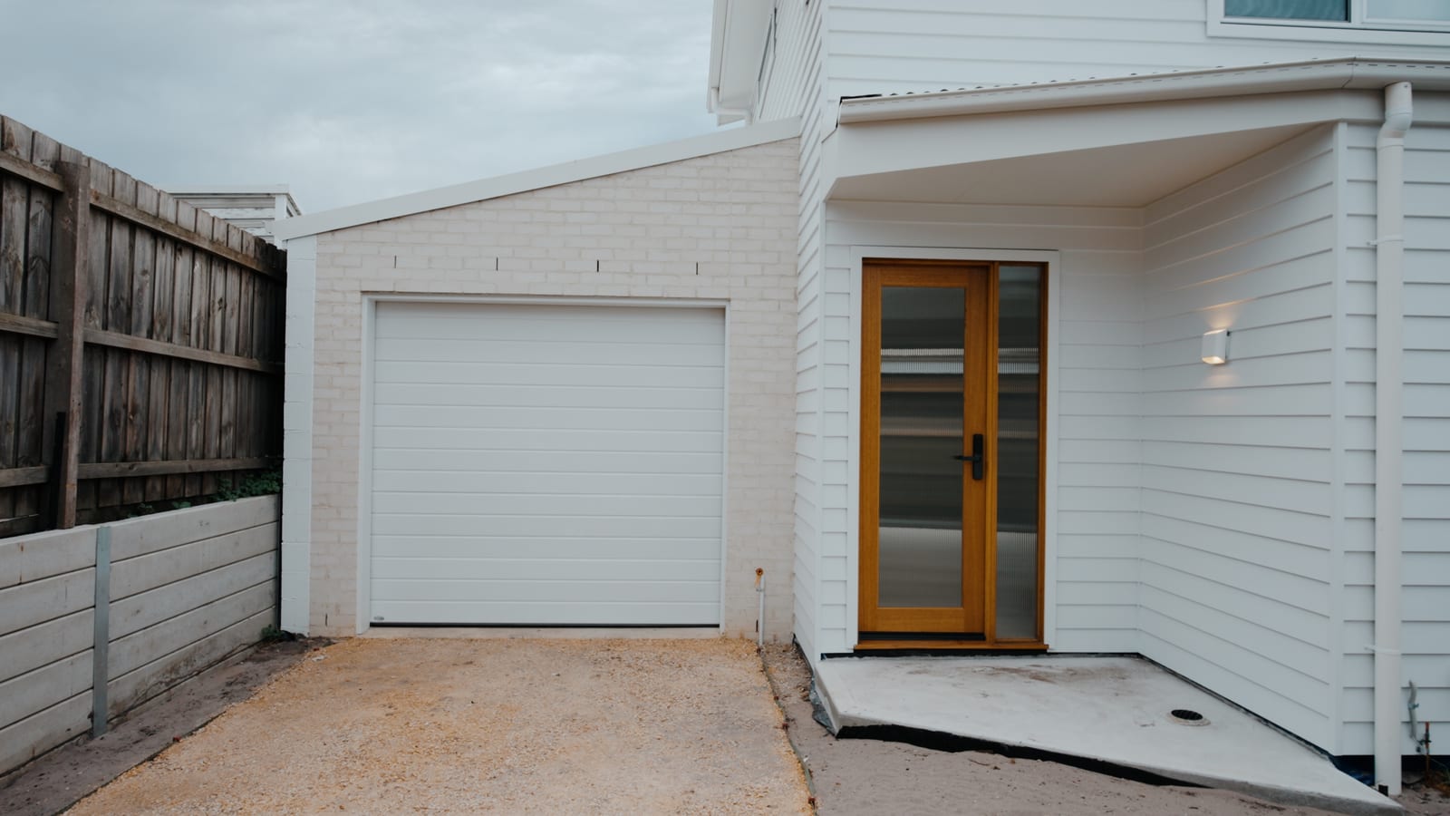 Garage door and timber entry door with concrete sleeper retaining wall running along the boundary