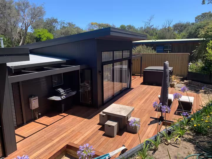 Deck with an outdoor kitchen area and spa under a pergola against dark cladding