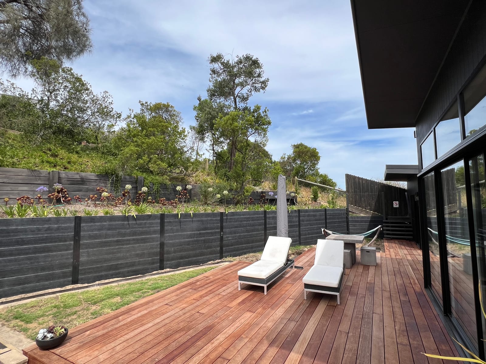 Hardwood deck with sun loungers against a dark boundary fence