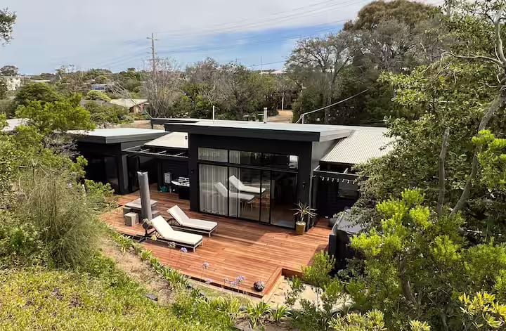 Elevated view of the finished home showing the dark roofline, deck and surrounding coastal scrub