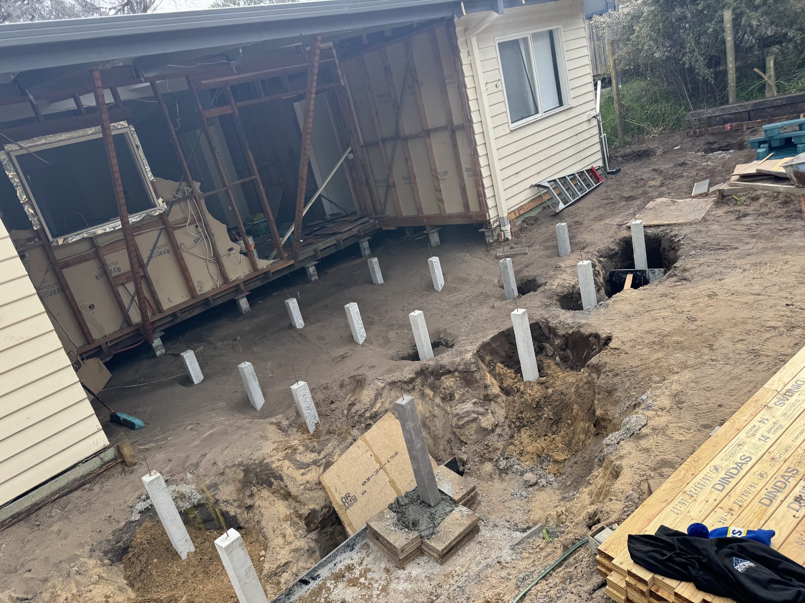 A renovation site mid-build, with new footings poured and insulation batts visible in the open wall frame