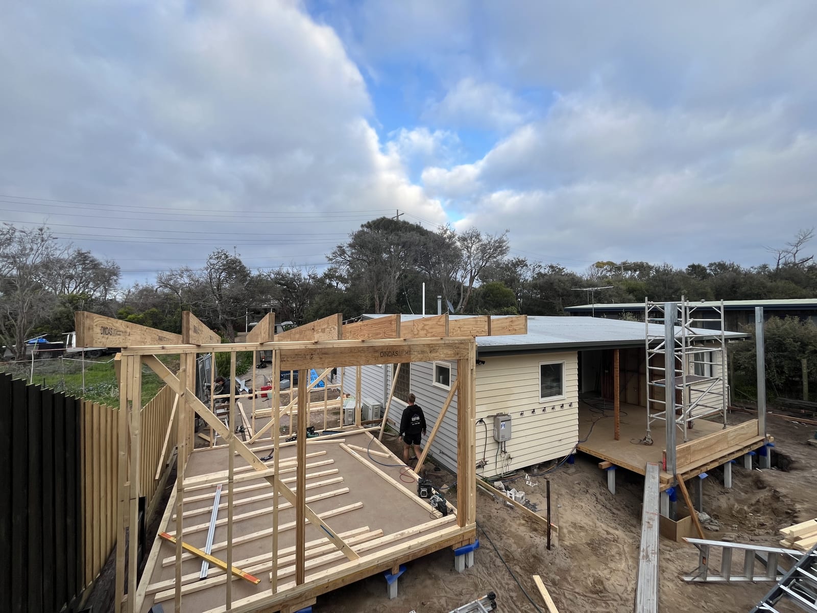 New timber framing rising against the original weatherboard house, roof rafters going on