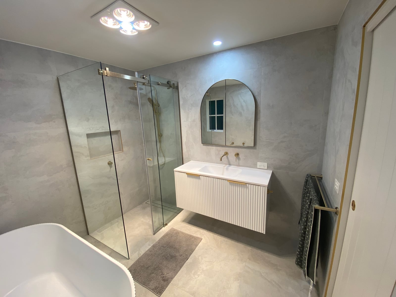 Fluted vanity and arched mirror in the main bathroom, with the shower beyond