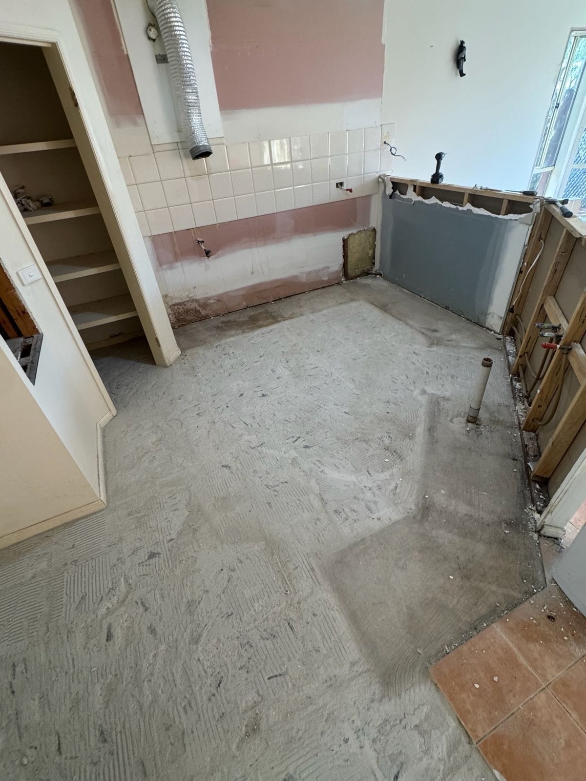 The old kitchen stripped out: cabinets gone, old wall tiles and pink paint still on the walls, the wall frame open on one side and the floor bare