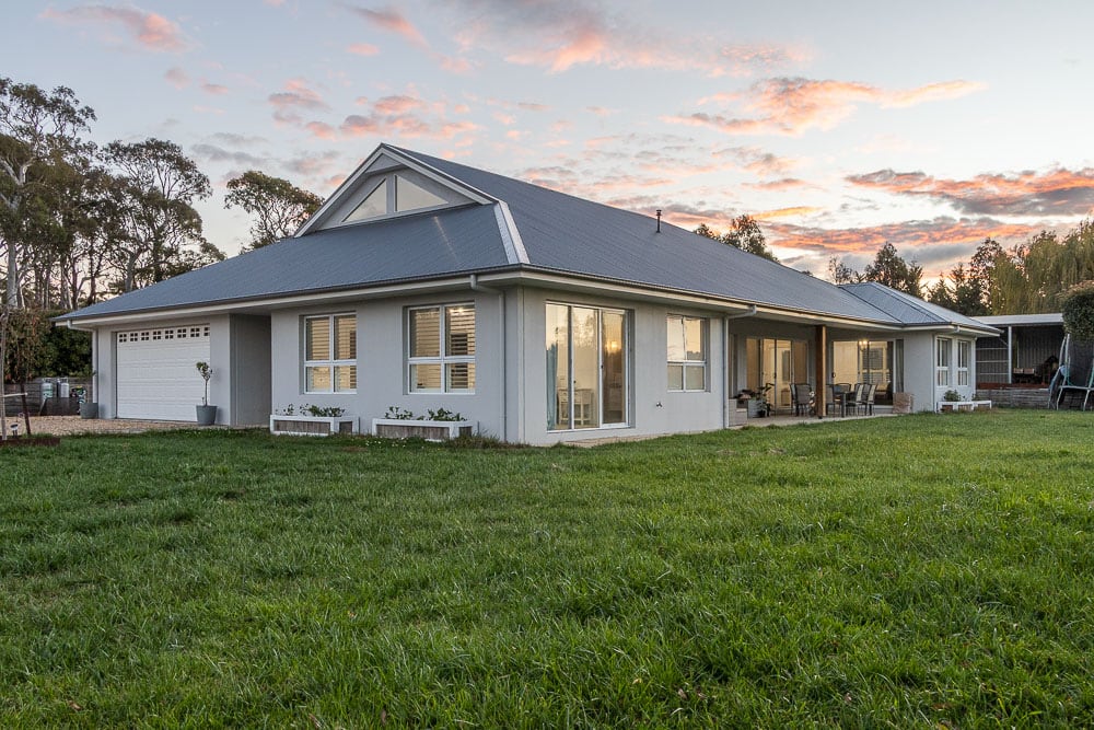 Completed single-storey precast concrete home with a hipped metal roof, rendered walls and a garage, on a large grassed block at dusk