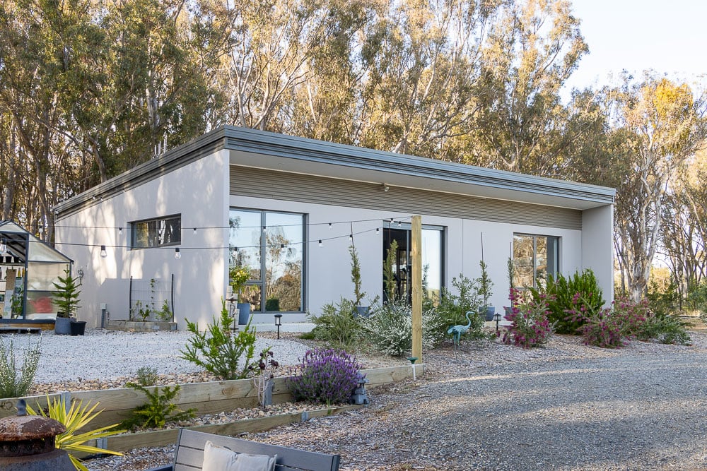Low-line precast concrete home with a skillion roof, full-height windows and a gravel garden among gum trees