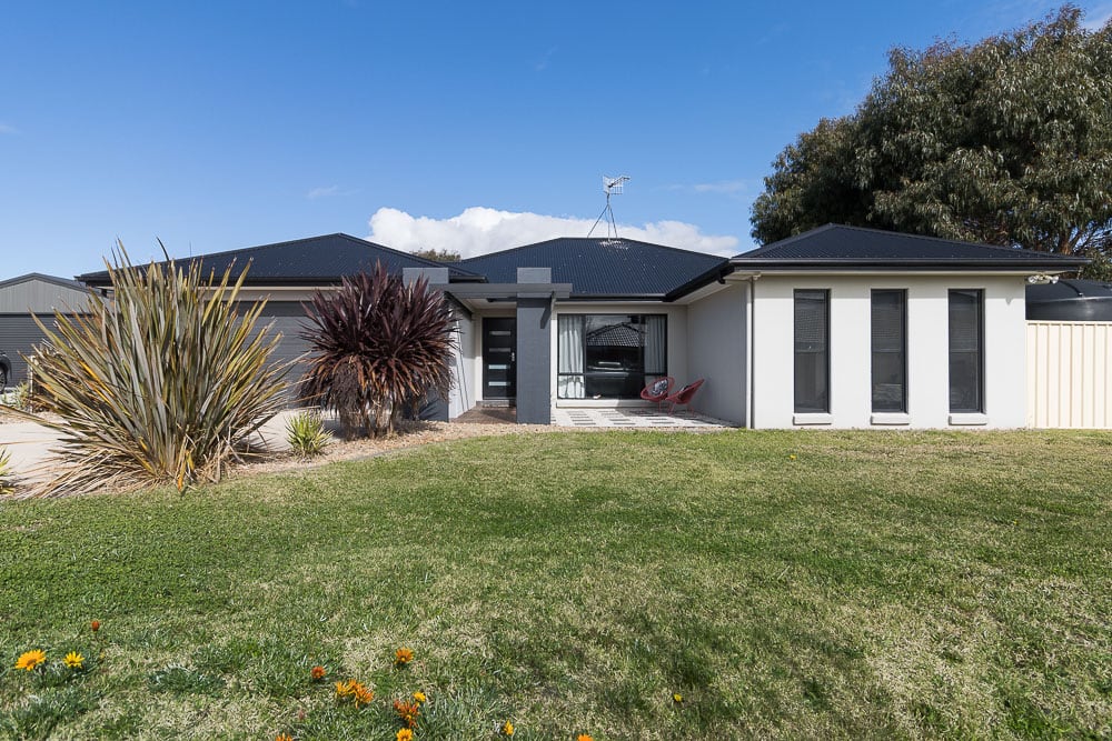 Precast concrete home with rendered walls, dark tiled roof and a feature entry portico, seen from the front lawn