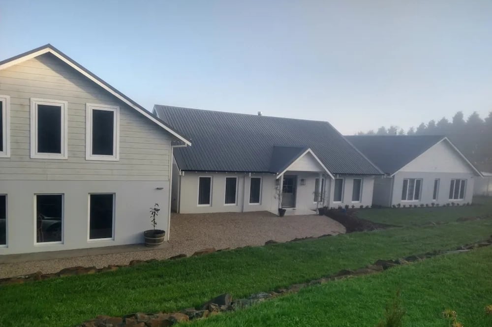 White weatherboard-look precast concrete home with steep gabled metal roofs and multi-pane windows, in a misty rural setting