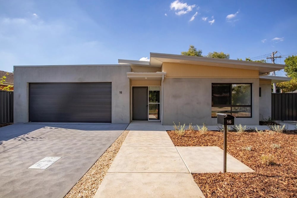 Contemporary single-storey precast concrete home with a double garage, skillion roof and grey render, with a landscaped front path
