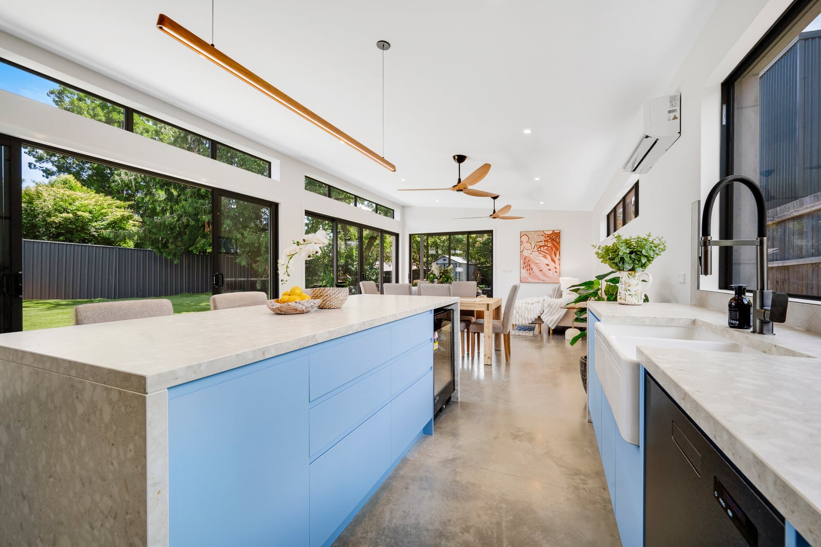 Interior of a completed precast concrete home: a bright open-plan kitchen and dining space with stone benchtops, polished concrete floor and full-height glazing to the garden