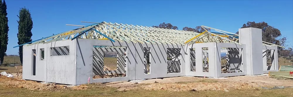 A precast concrete home part way through construction: engineered wall panels standing and propped, with all roof trusses craned into position above them