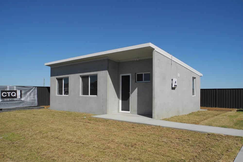 A completed precast concrete cold shell: bare grey panels, roof on, windows and door in, standing on a finished slab