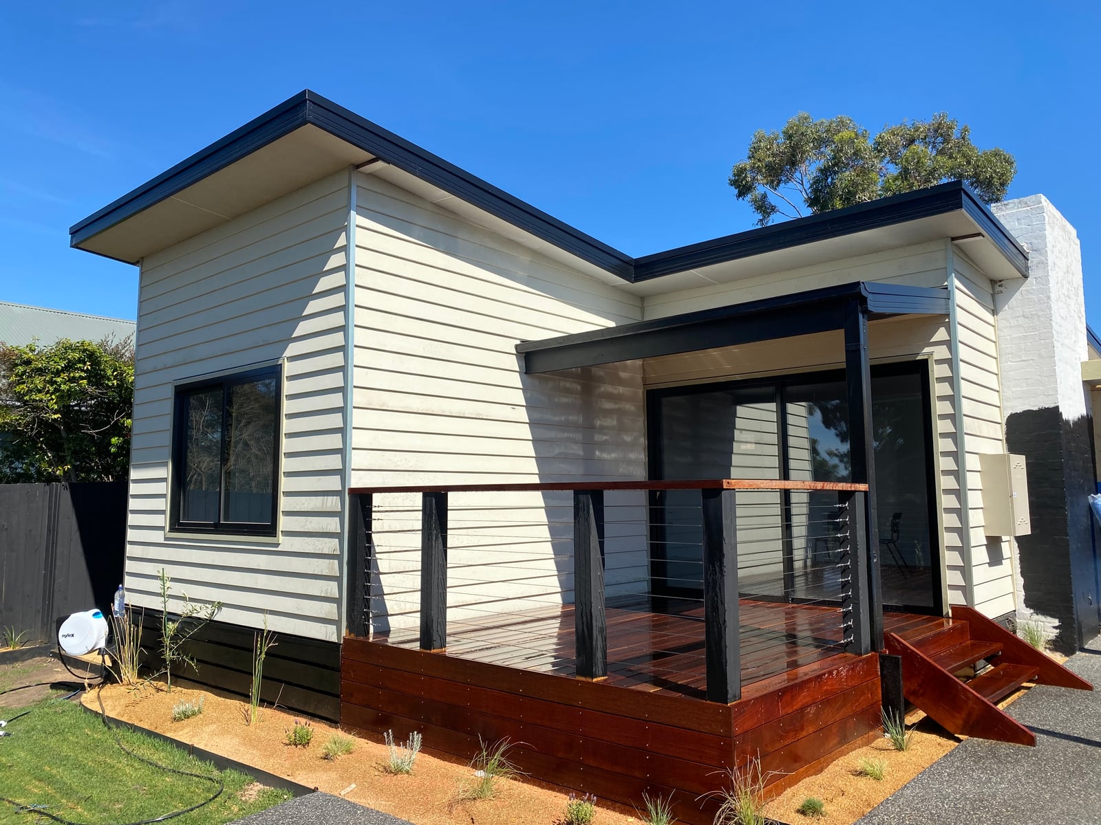 Completed McCrae addition in cream weatherboard with a skillion roof, hardwood deck and black cable balustrade