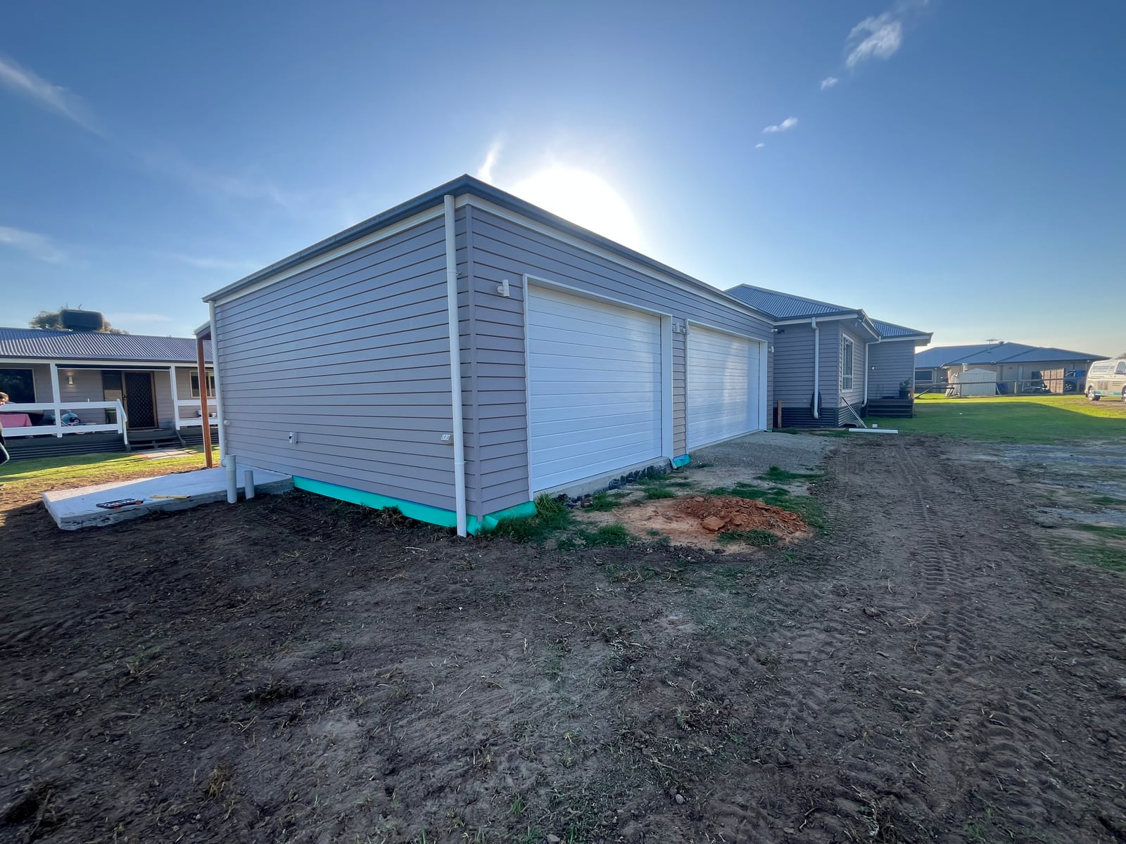 Completed triple garage clad in weatherboard with three white roller doors, attached to a single-storey home